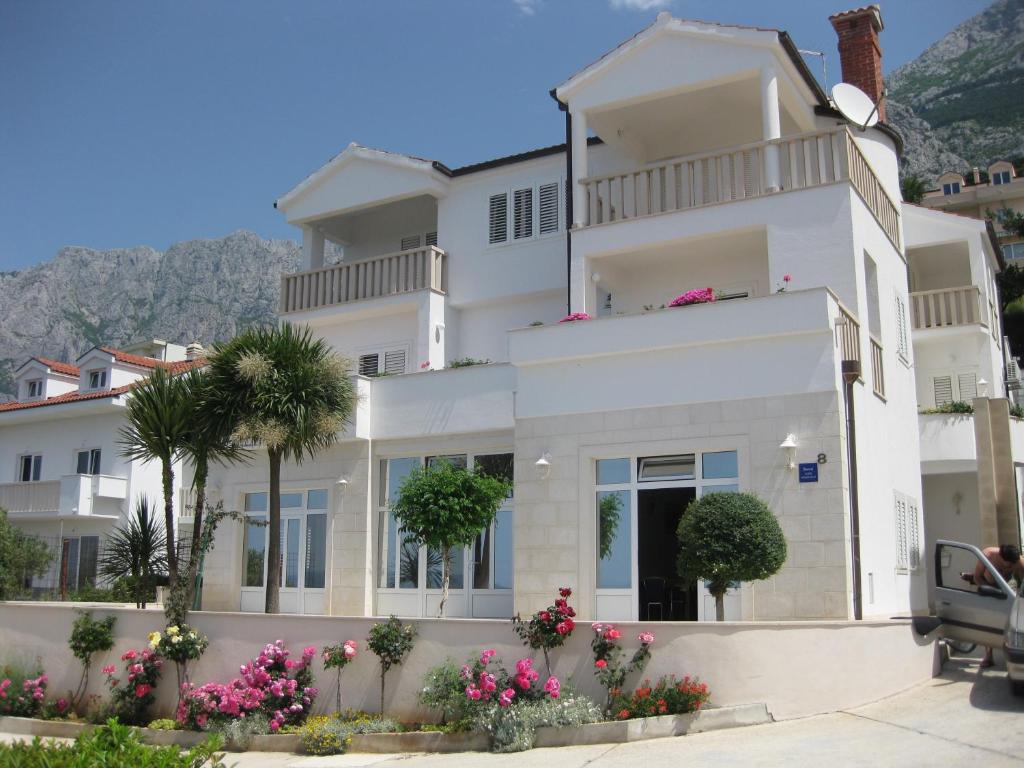 un grand bâtiment blanc avec des palmiers et des fleurs dans l'établissement Villa Ruza, à Makarska