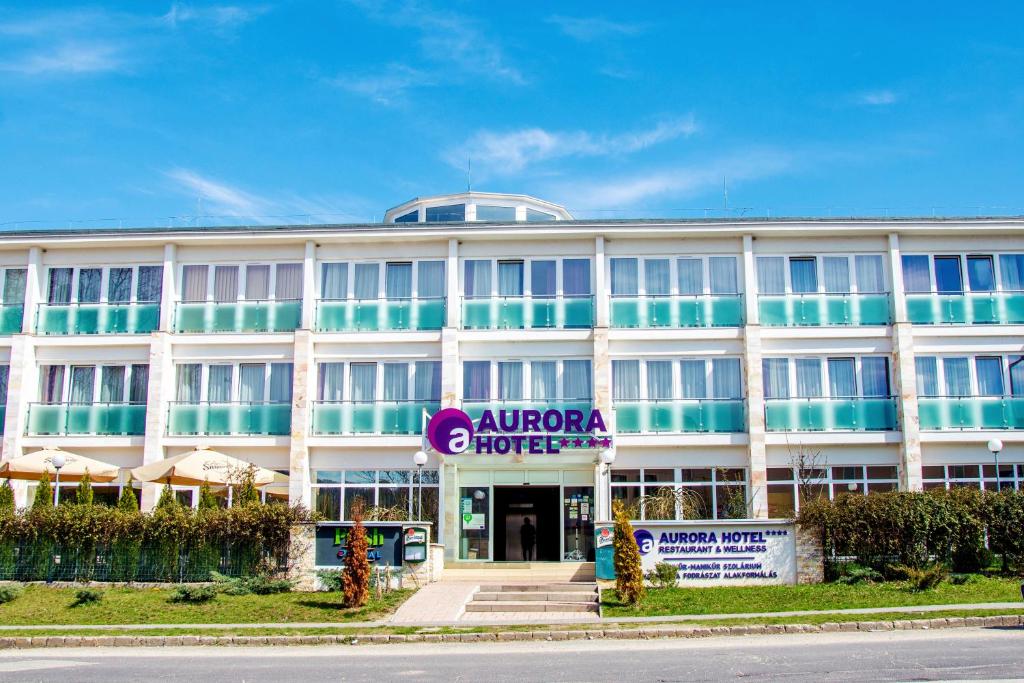 een groot wit gebouw met een bord ervoor bij Hotel Aurora in Miskolctapolca