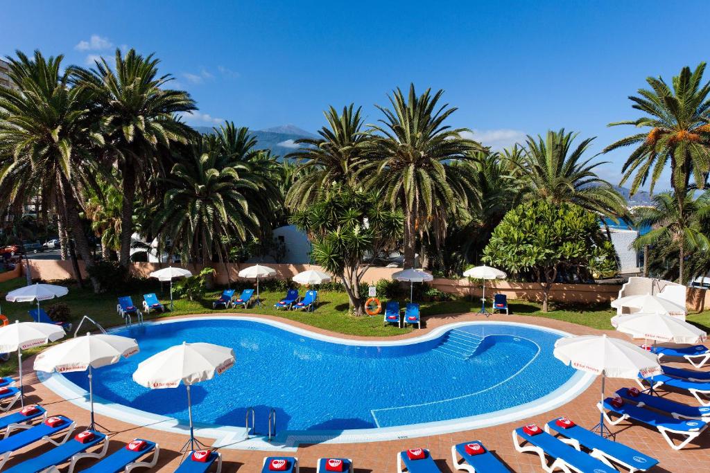 una piscina con sillas, sombrillas y palmeras en Sol Puerto de la Cruz Tenerife en Puerto de la Cruz