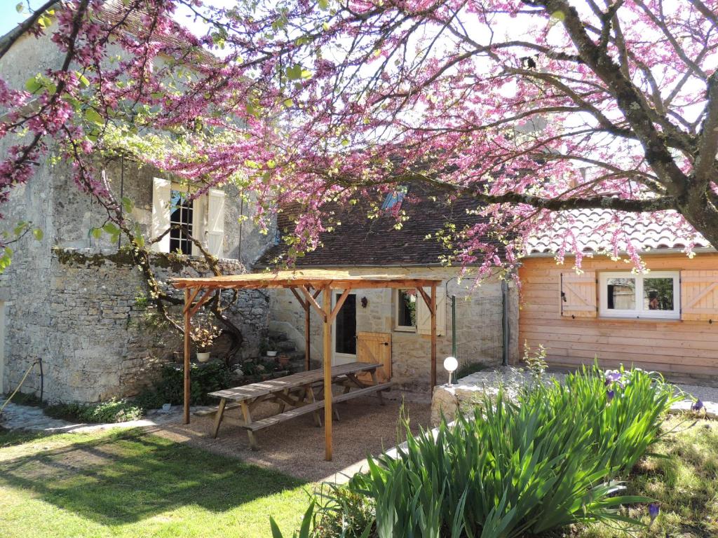 un tavolo da picnic di fronte a una casa con un albero con fiori rosa di Le Pigeonnier a Martel