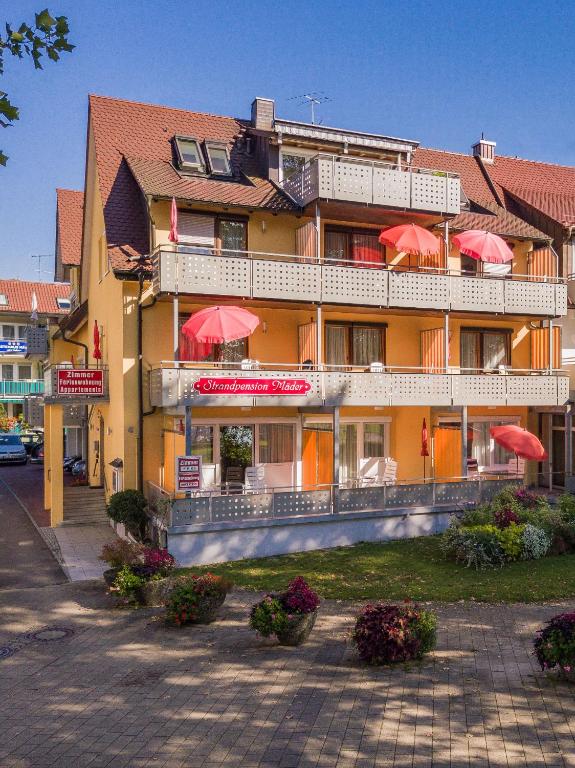 a large hotel with red umbrellas in front of it at Strandpension Mäder in Uhldingen-Mühlhofen