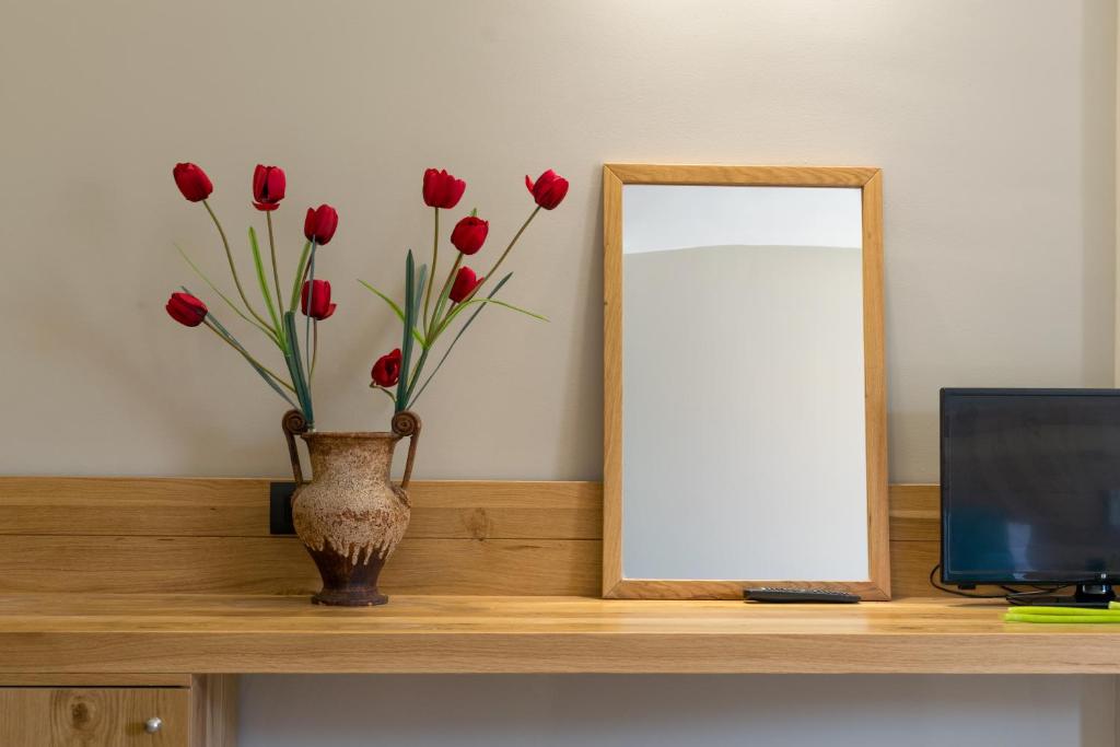 a mirror and a vase with red flowers on a desk at Bali Diamond "by Checkin" Adults Only in Bali