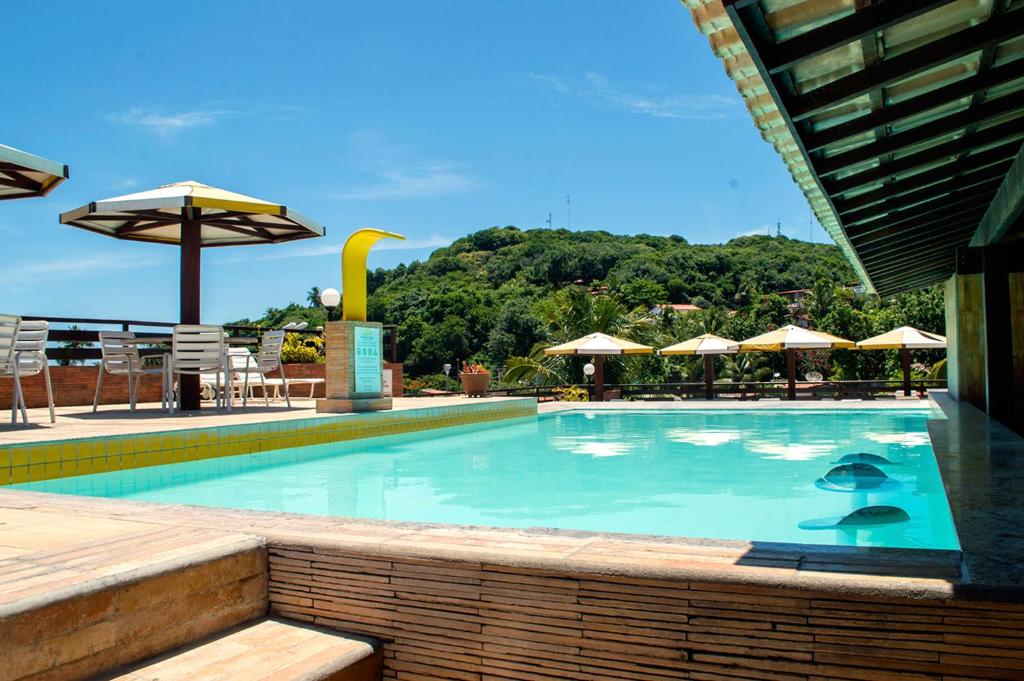 a large swimming pool with chairs and umbrellas at Apartamento Pipa Deluxe in Pipa