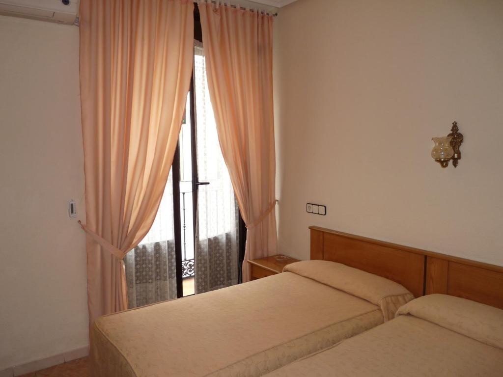 a bedroom with two beds and a window with curtains at Hostal Fernandez in Madrid