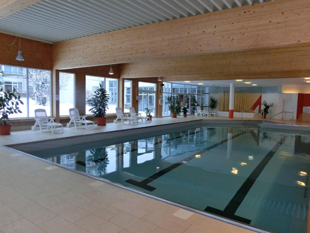 a large swimming pool in a building with white chairs at Haus Bergland in Neureichenau