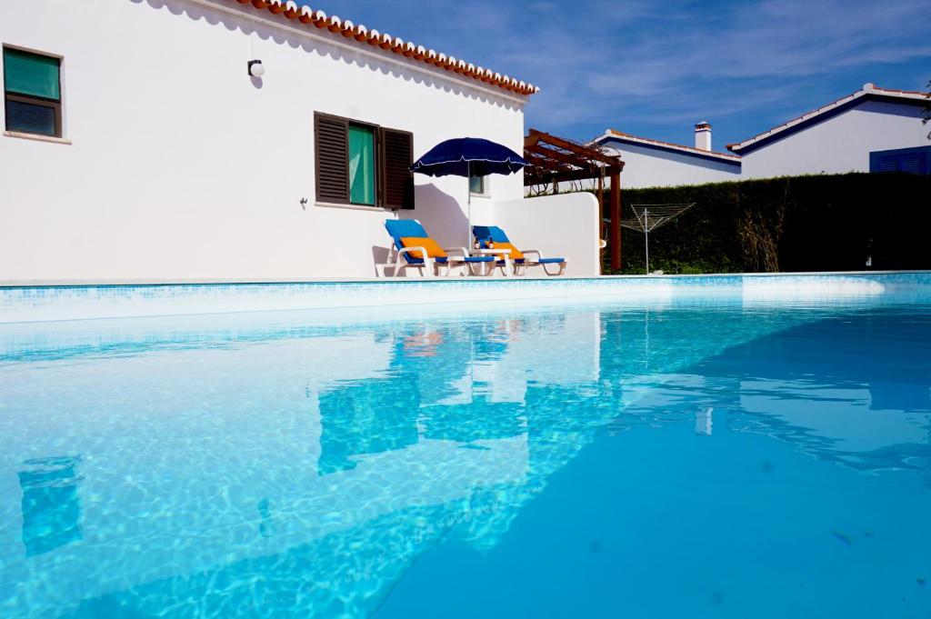 a pool with two chairs and an umbrella next to a house at Casa Tucano in Aljezur