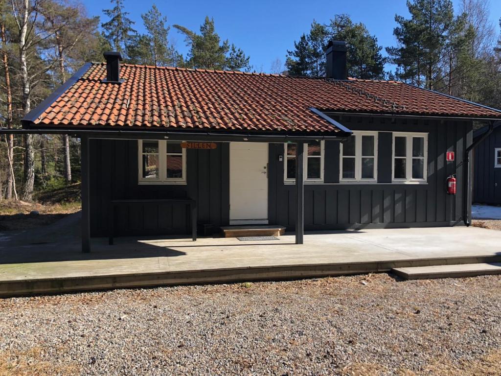 uma pequena casa preta com um telhado vermelho em Hällestrand Cottage -Sillen em Strömstad