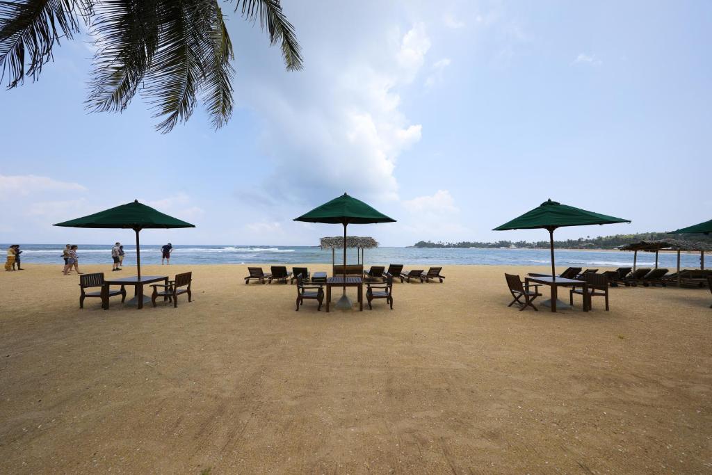 una playa de arena con mesas, sillas y sombrillas en Joe's Resort Unawatuna, en Unawatuna