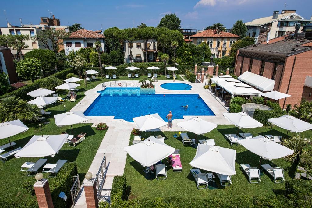 DB Villas Le Ville del Lido Resort في ليدو دي فينيتسا: اطلالة علوية على مسبح مع مظلات بيضاء