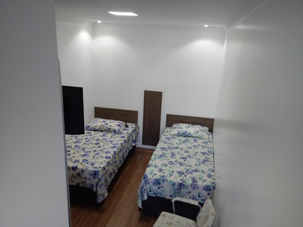 a room with two beds and a tv on the wall at Mini Kitnet - Santa Cruz do Sul in Santa Cruz do Sul