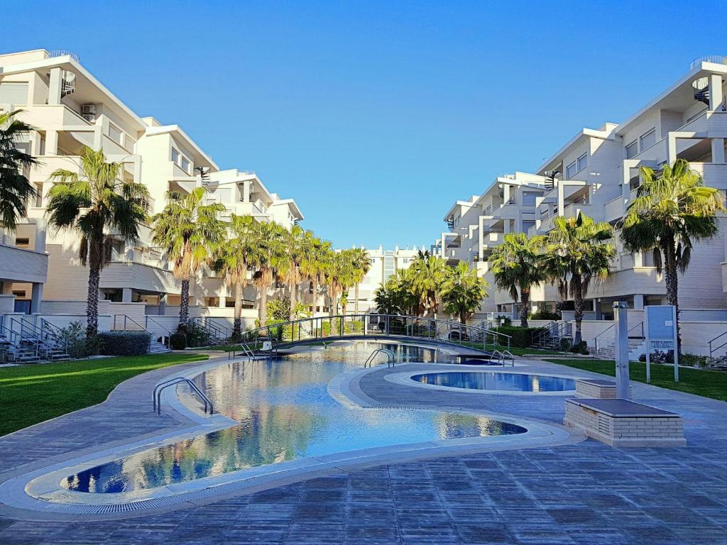 a swimming pool in front of a building with palm trees at Apartamento ELEGANCE Siesta - DENIA in Denia