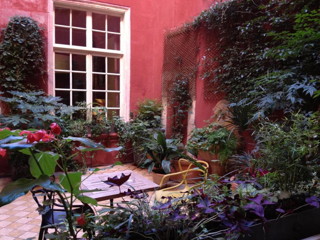 a garden in front of a red building with a table and flowers at Hôtel de l'Amphithéâtre in Arles