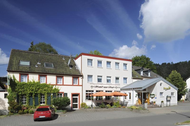 ein rotes Auto, das vor einem weißen Gebäude parkt in der Unterkunft Hotel zur Post in Deudesfeld