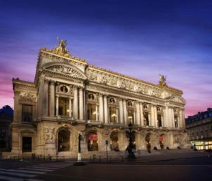 a large white building with a sunset in the background at Hôtel Royal Opéra in Paris