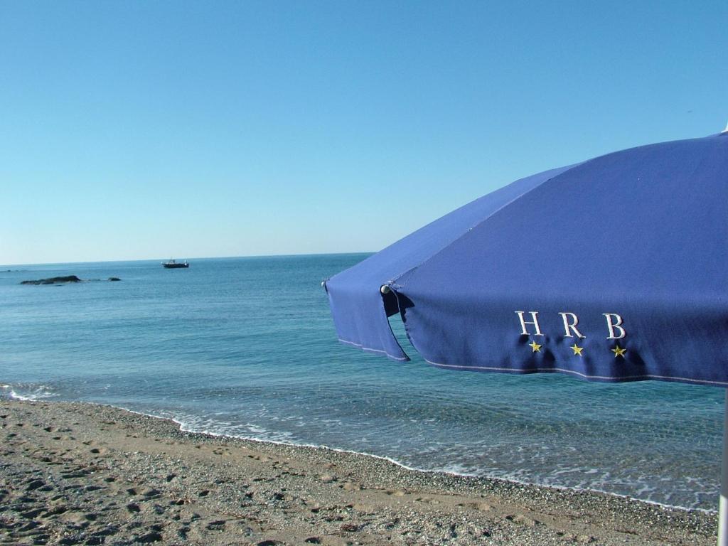 um guarda-sol azul sentado numa praia perto do oceano em Hotel Riviera Bleu em Diamante