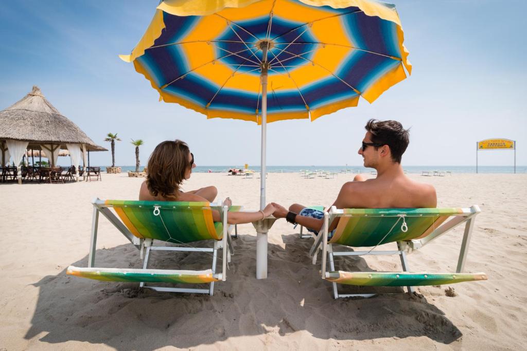 two people sitting in chairs under an umbrella on the beach at Hotel Mediterraneo in Sottomarina