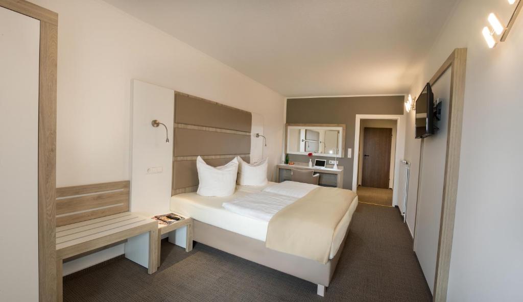 ein Hotelzimmer mit einem großen weißen Bett und einer Bank in der Unterkunft Confour Hotel in Burgdorf