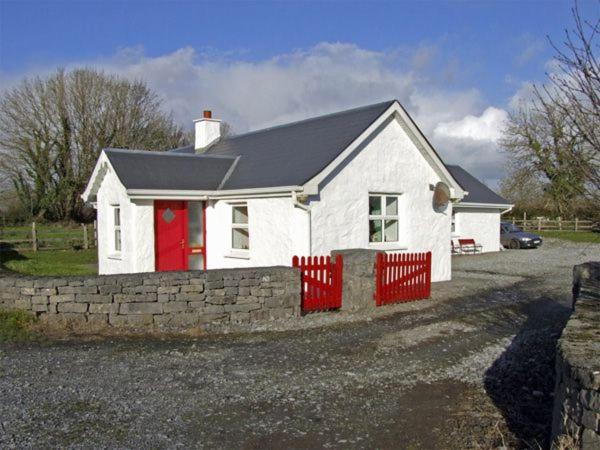a white house with a red fence in a driveway at Delia's Cottage in Ballinrobe