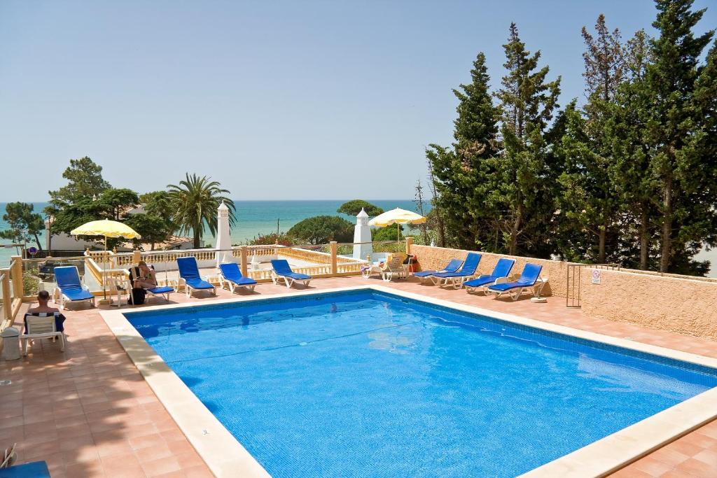 einen Pool mit Stühlen und das Meer im Hintergrund in der Unterkunft Apartamentos Do Parque in Albufeira