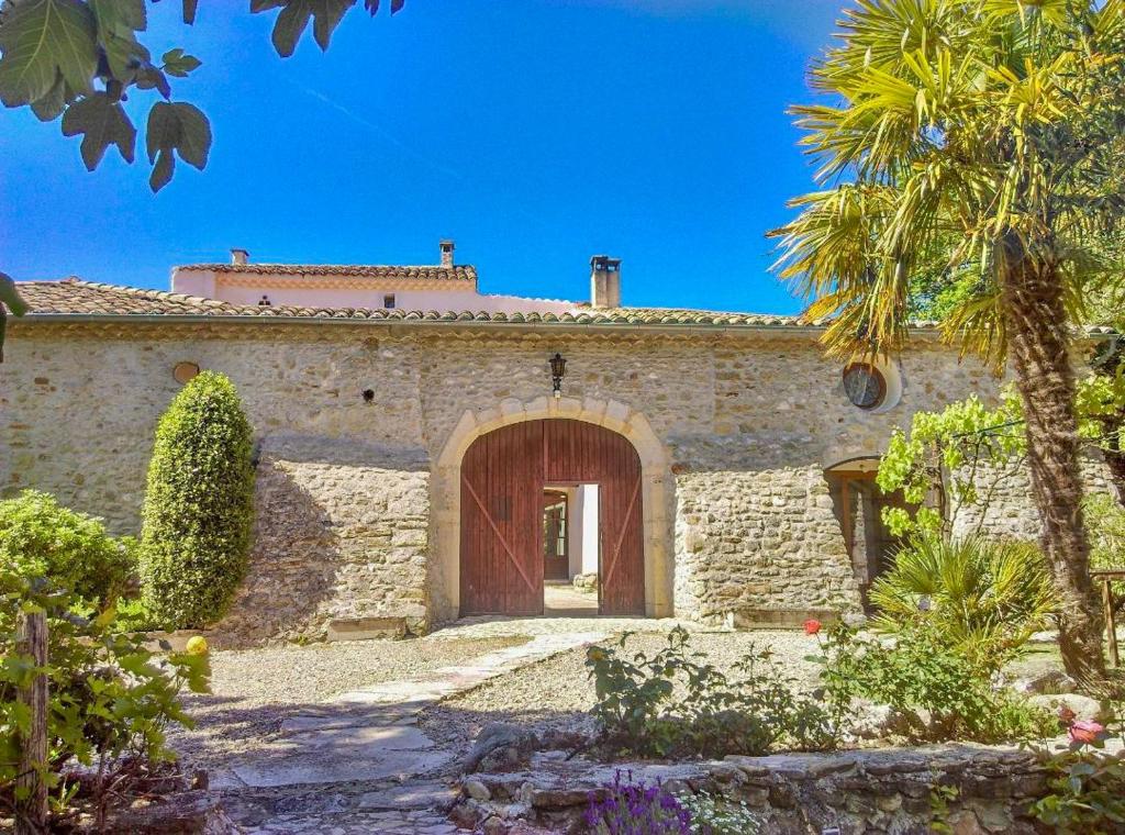 une maison en pierre avec une grande porte et un palmier dans l'établissement La Bastide De Sauvetas, à Bonlieu-sur-Roubion
