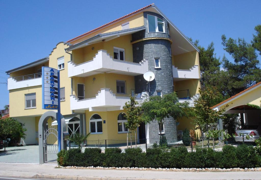 een geel en wit gebouw met bomen ervoor bij Apartments San in Sukošan