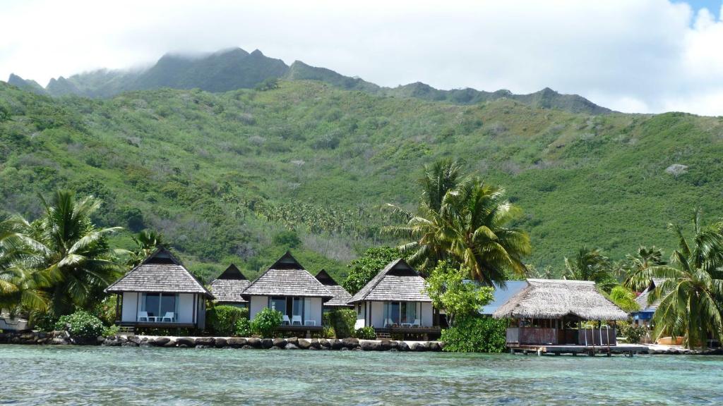 a row of houses on the water with mountains in the background at Pension Motu Iti in Pihaena
