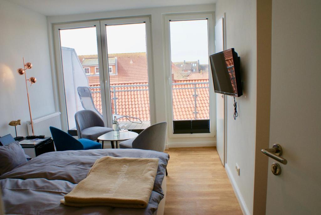 a bedroom with a bed and a tv and a balcony at Deichhotel Rose in Juist