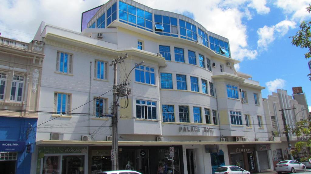a large white building with blue windows on a street at Palace Hotel in Araguari