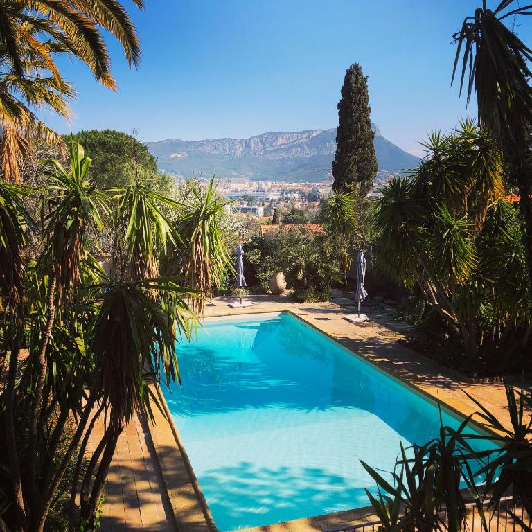 a swimming pool with palm trees and a mountain in the background at Les Bastidieres - Cap Brun in Toulon