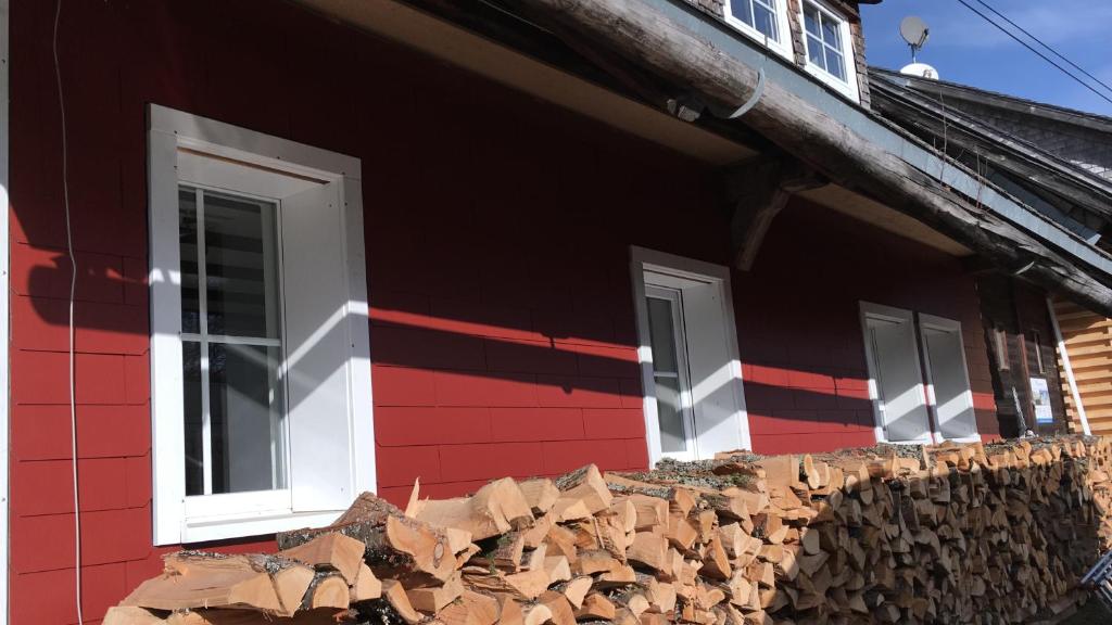 a red building with white windows and a pile of wood at Apartment im Schwarzwaldhaus in Schluchsee