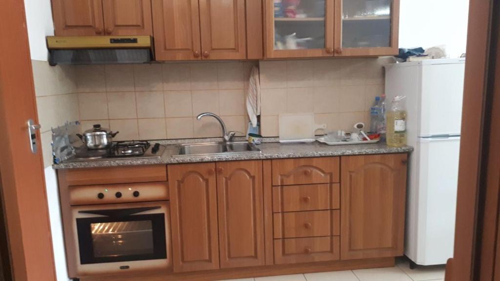 La cuisine est équipée de placards en bois, d'un évier et d'un réfrigérateur. dans l'établissement Geni Apartment, à Durrës