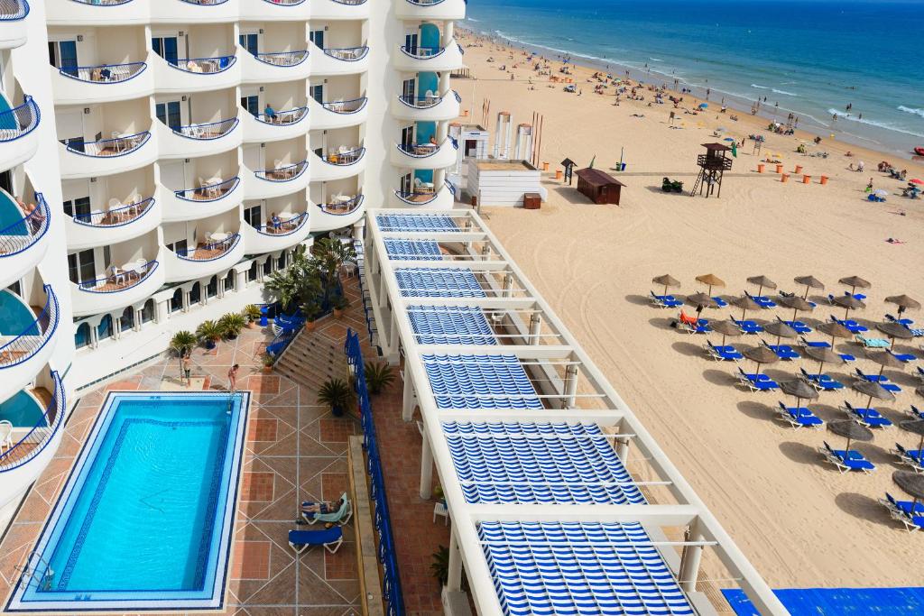 a building with a swimming pool next to a beach at Hotel Playa Victoria in Cádiz