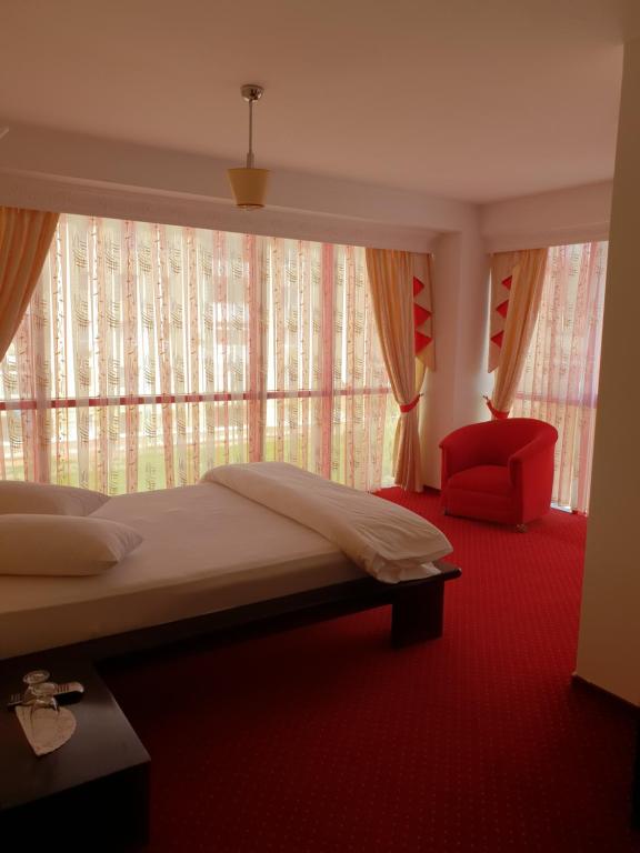 a bedroom with a bed and a red chair and a window at Pensiunea Ghiocela in Motru