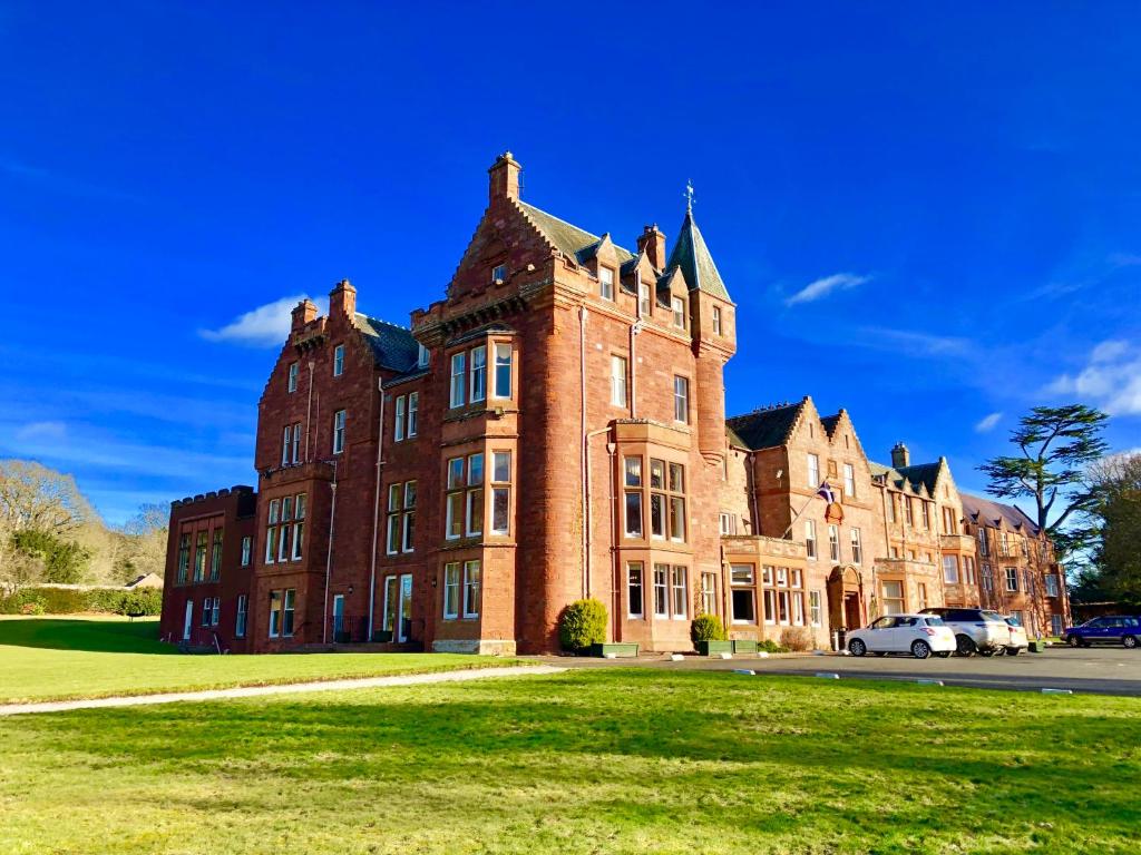 um grande edifício de tijolos vermelhos com carros estacionados na frente em Dryburgh Abbey Hotel em Melrose