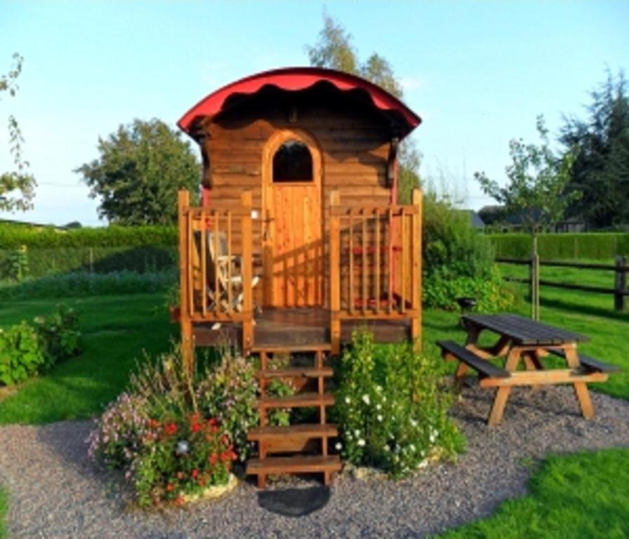 a wooden play house with a bench and a picnic table at La Roulotte du Verger in Barneville-sur-Seine