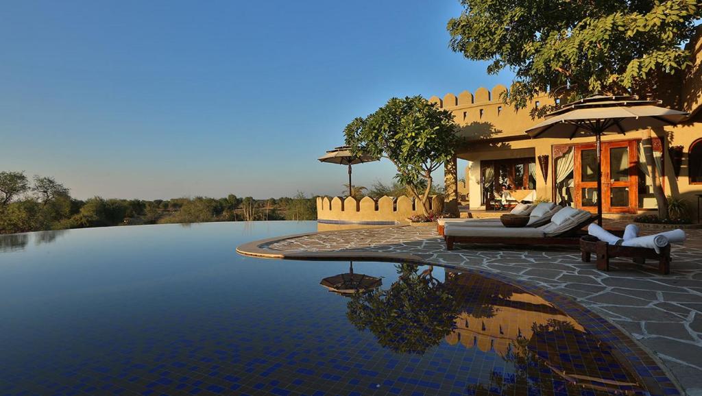 a swimming pool with a couch and chairs next to a house at Mihir Garh in Rohat