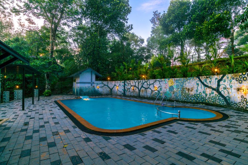 a swimming pool in a backyard with a stone wall at Letstay Adithya Nature Resort & Spa in Vythiri