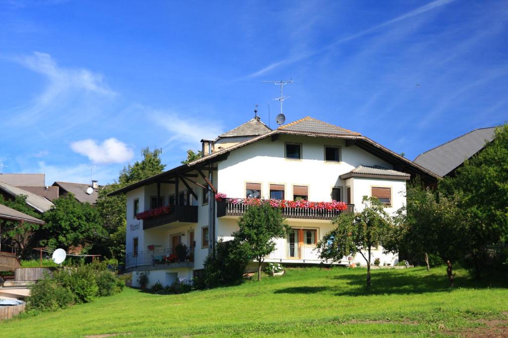 une maison blanche avec des fleurs rouges sur le balcon dans l'établissement Mairhof, à Laion