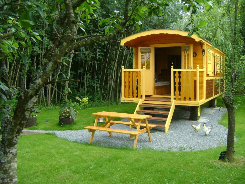 una casa de juegos amarilla con una mesa de picnic y un banco en Les Roulottes de Saint-Sulpice en Saint-Sulpice-en-Pareds