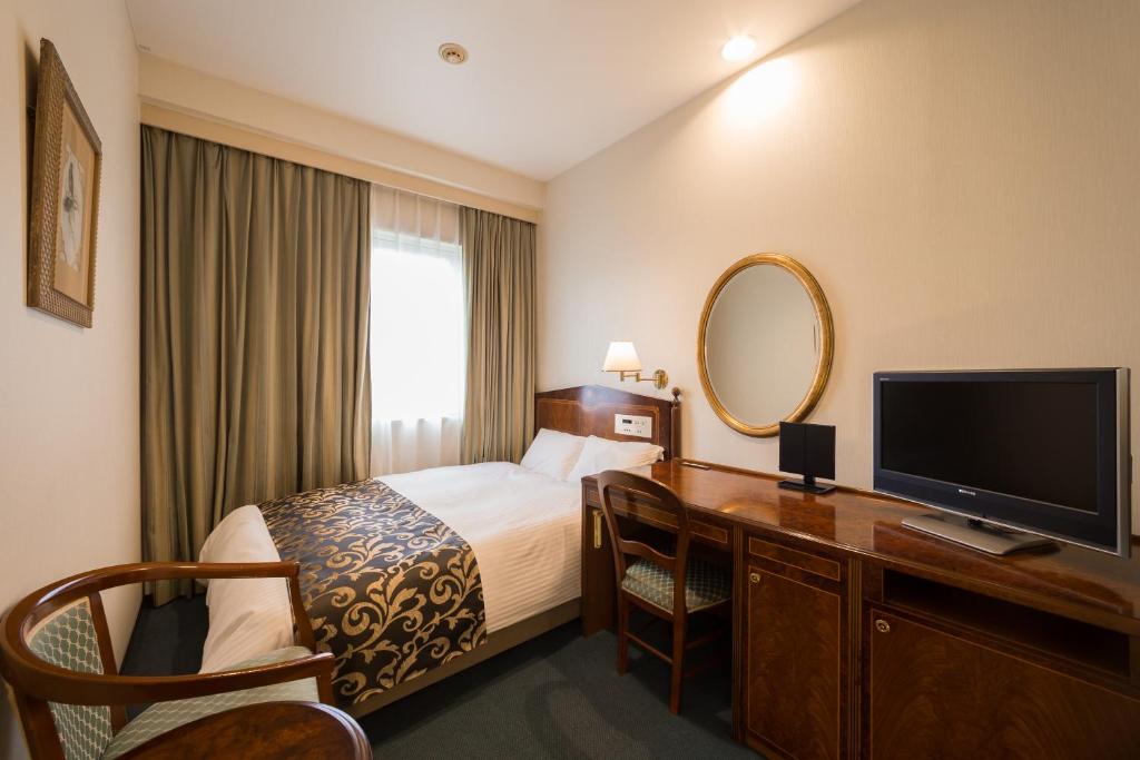 ein Hotelzimmer mit einem Bett und einem Schreibtisch mit einem TV in der Unterkunft Dukes Hotel Nakasu in Fukuoka