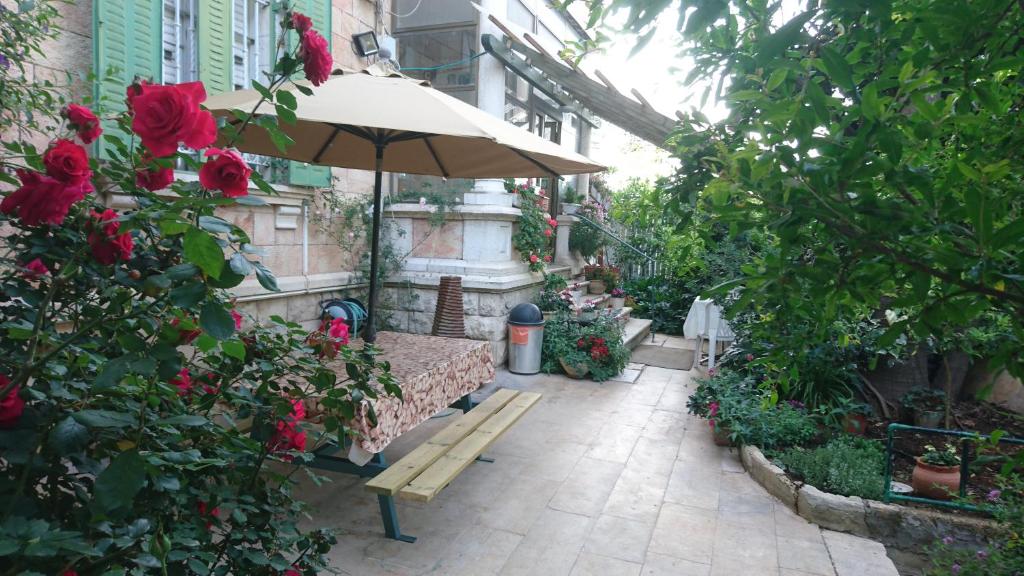 a patio with a table and an umbrella and roses at Allenby2 B&B in Jerusalem