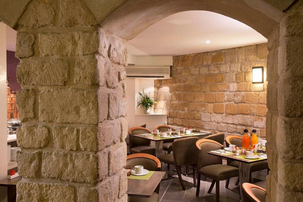 a restaurant with tables and chairs and a stone wall at Hotel Elysa-Luxembourg in Paris
