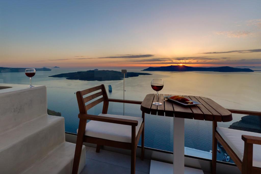 a table with two glasses of wine on a balcony at Iriana Suites in Fira