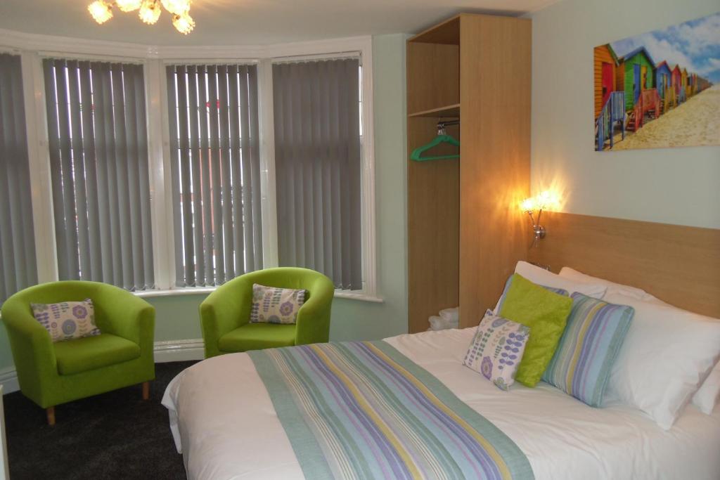 a bedroom with a bed and two green chairs at The Beaucliffe in Blackpool
