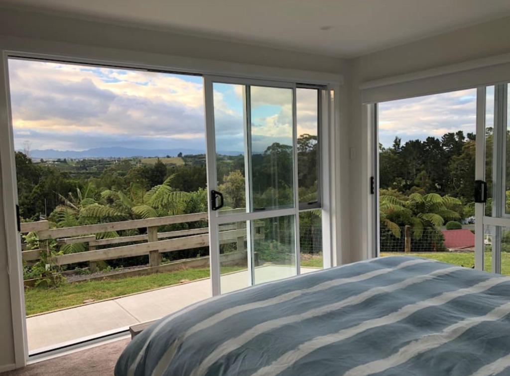 a bedroom with a large window looking out at the forest at Minden Meadows Retreat in Tauranga