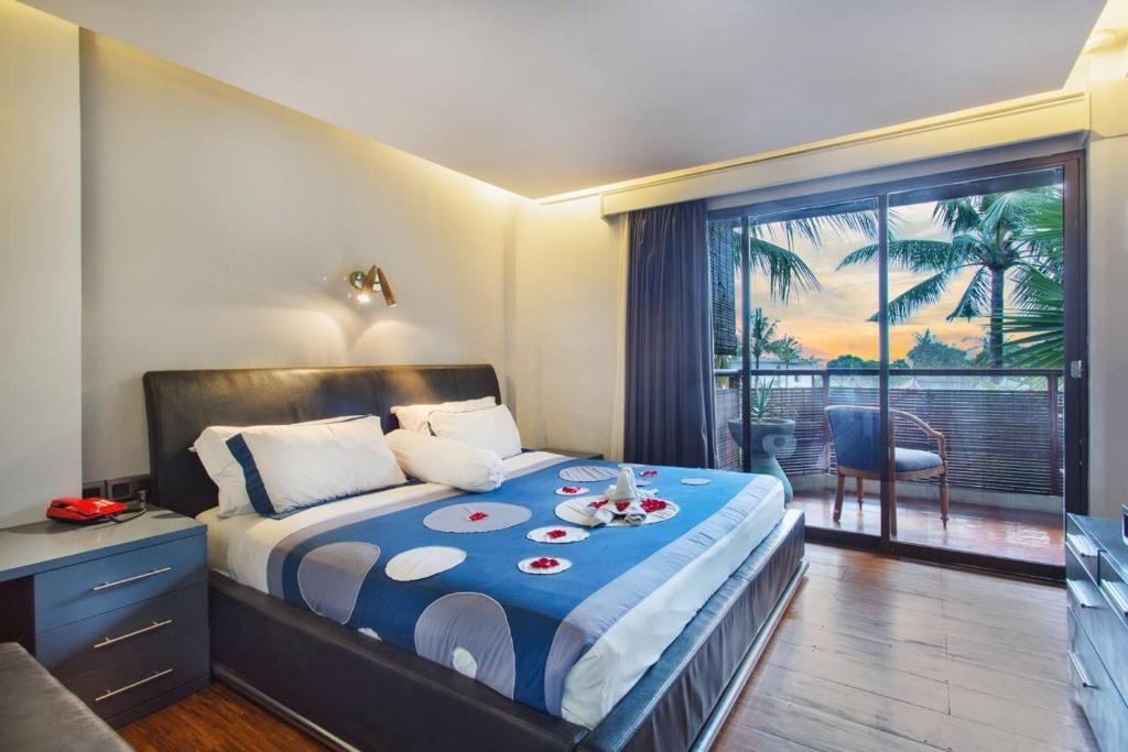 a bedroom with a bed with a blue comforter and a balcony at Sejuk Suites in Legian