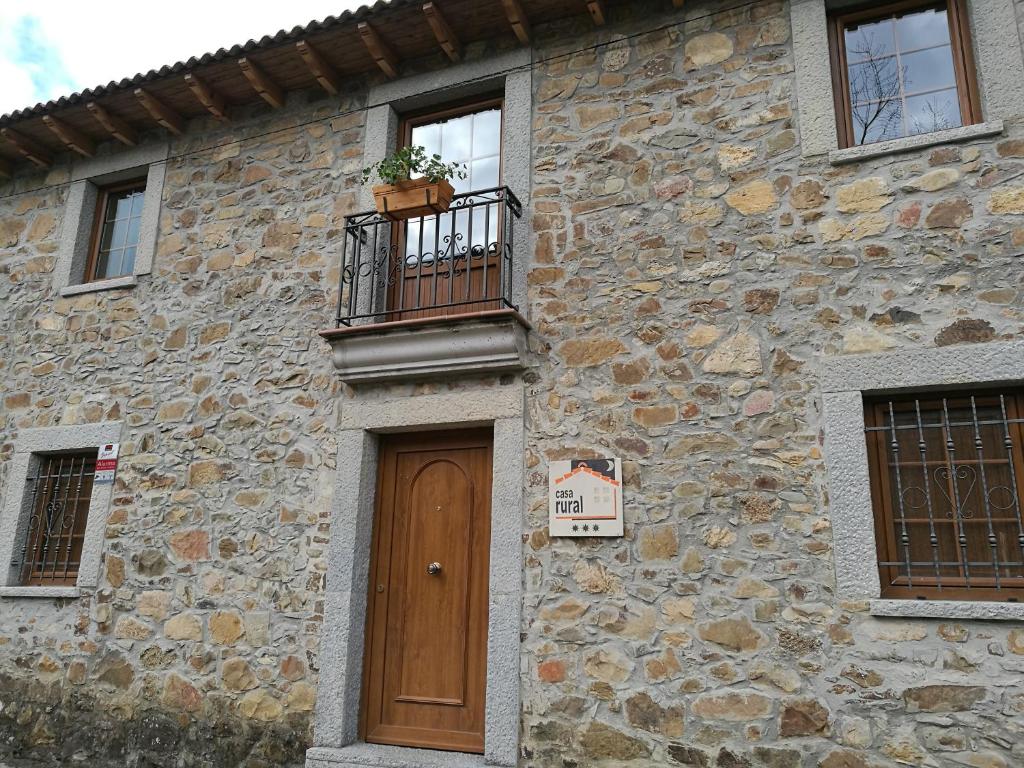 un edificio de piedra con puerta de madera y balcón en Casa Rural Sensaciones 3 dormitorios con jardin, en Carrocera