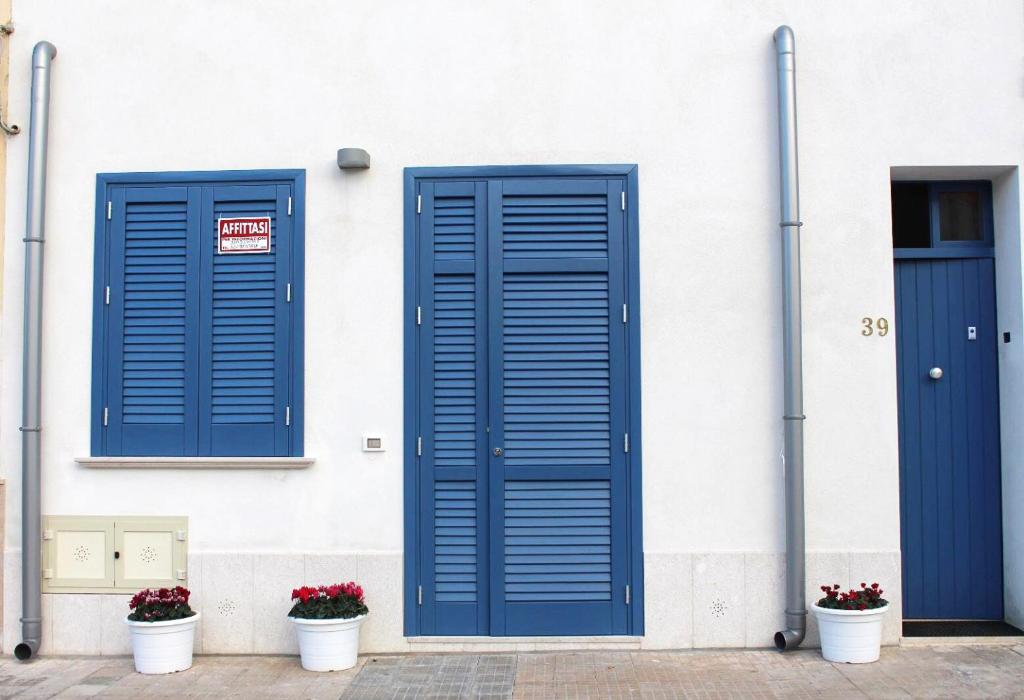 three blue doors on a white building with flower pots at Casetta Maremè in San Vito lo Capo