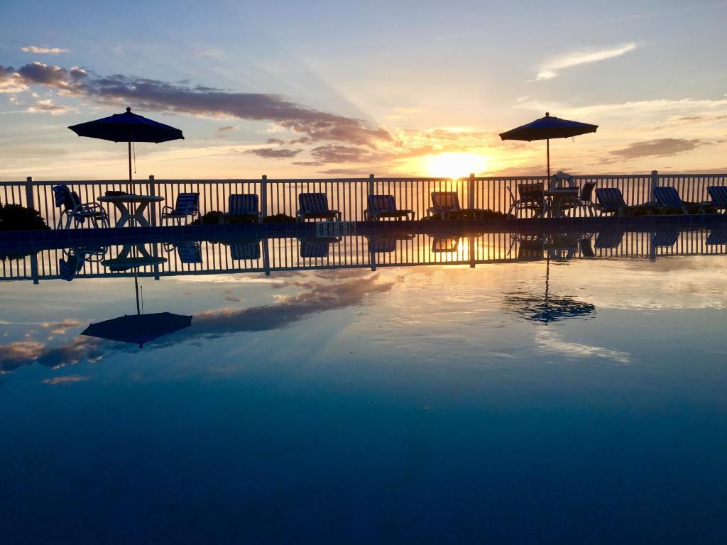 una piscina con sillas y sombrillas frente a la puesta de sol en Coral Sands Inn, en Ormond Beach
