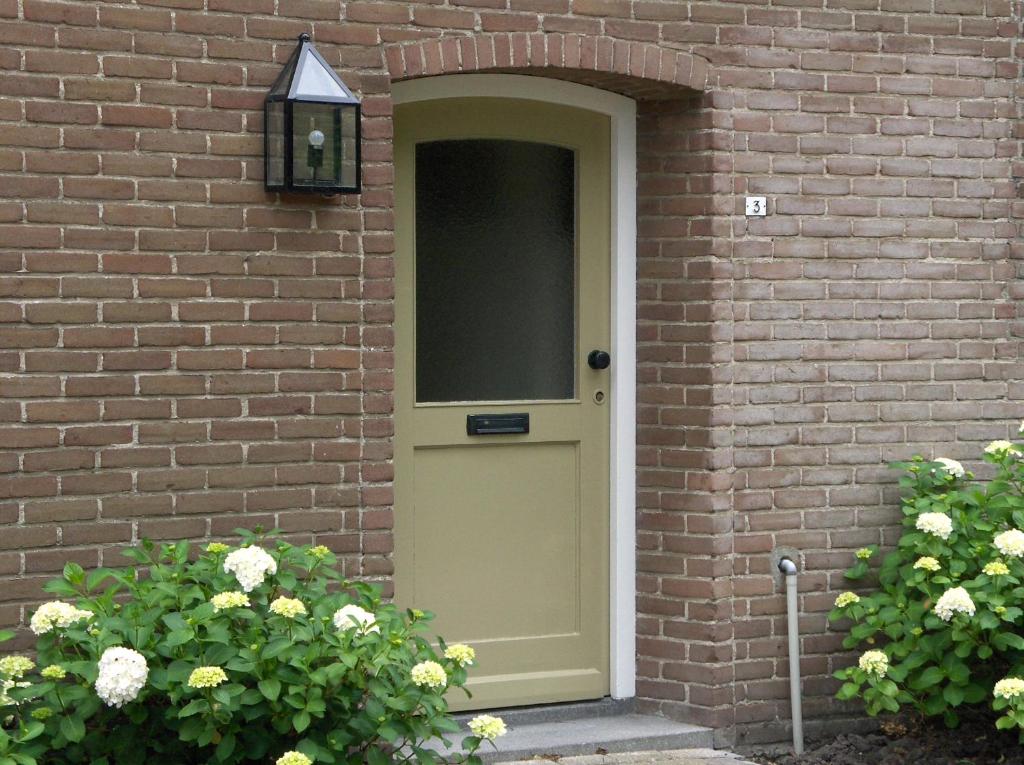 una puerta verde en una pared de ladrillo con flores en de Paardenmarkt, en Aardenburg